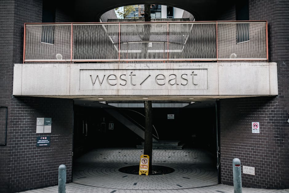 Exterior view of a multi-story red brick building with white decorative elements and black iron balconies on the upper floors, situated along a paved street in West Hampstead. The building features la