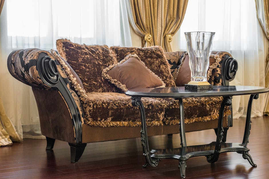 A close-up view of a polished wooden table with a warm, natural finish, positioned upright in a well-lit room. To the left, three green upholstered chairs with rounded backs and smooth fabric are arra