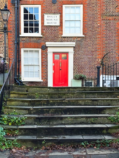 Exterior view of a traditional brick residential building with a white sign reading 'Holly Mount House' mounted between two sash windows on the upper floor. The building features a striking red front 